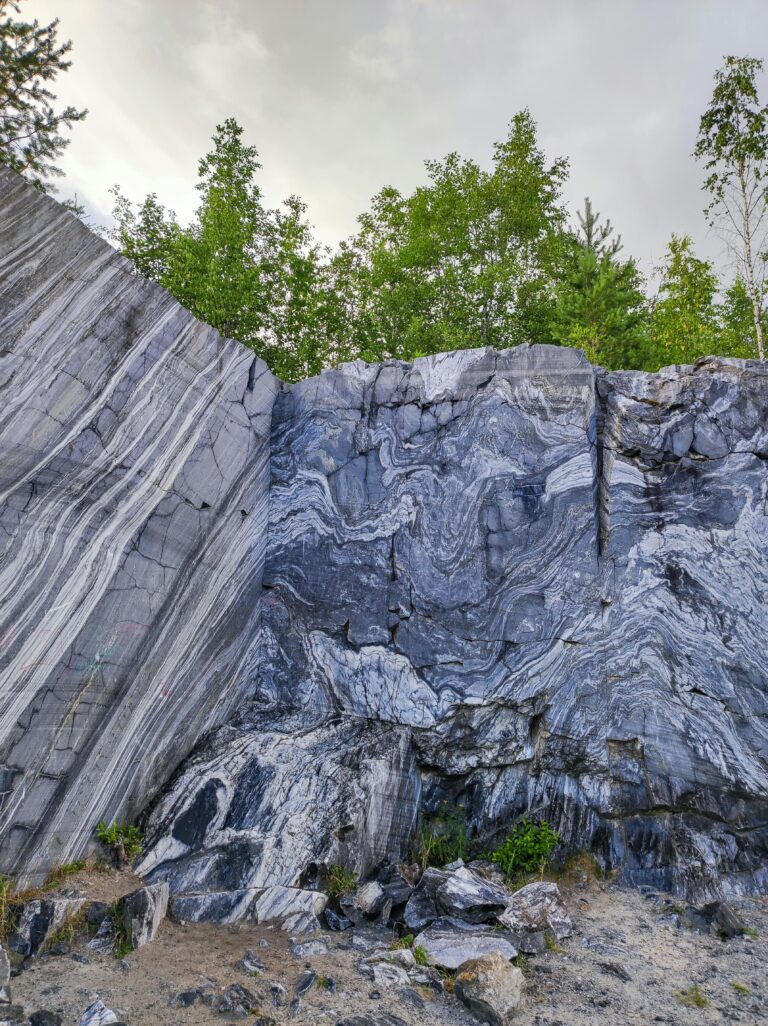 Dramatic marble rock formation in a lush forest setting, showcasing stunning natural patterns.
